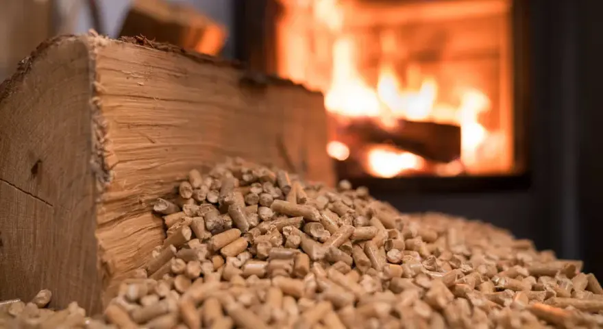 Bûches et granulés de bois, prêts pour une chaudière bois mixte. Le feu crépite en arrière-plan.