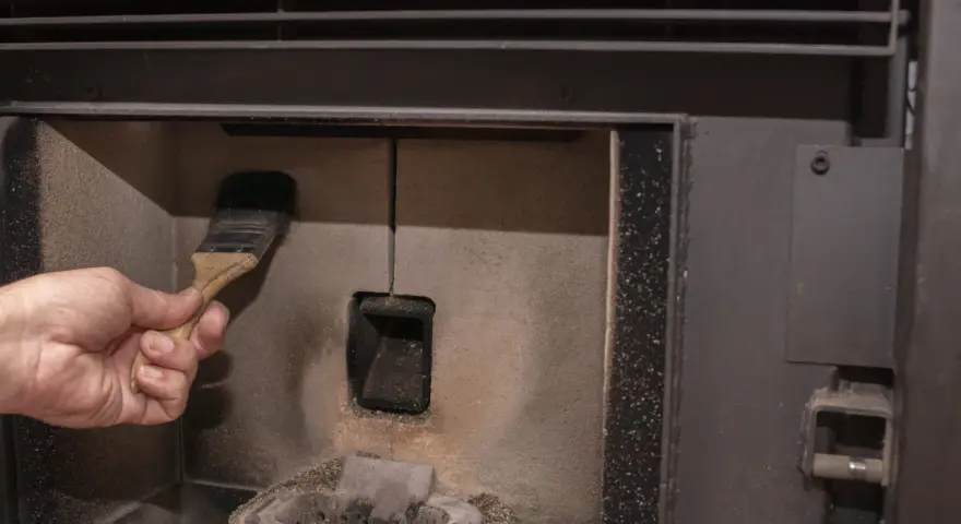 Main d'une personne nettoyant la chambre de combustion d'un poêle à pellet MCZ avec une brosse. Un problème de nettoyage peut causer des dysfonctionnements.