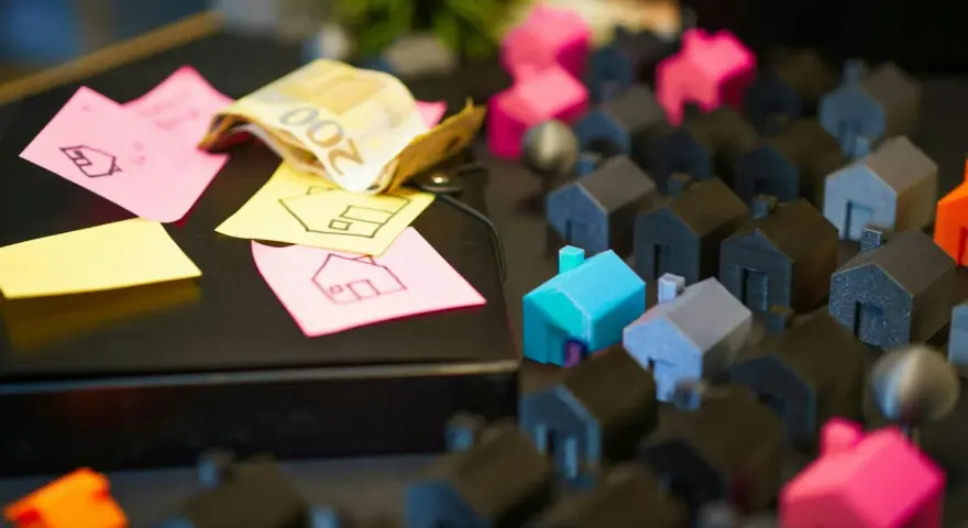 Petites maisons miniatures, billets de banque et post-its avec des dessins de maisons.
