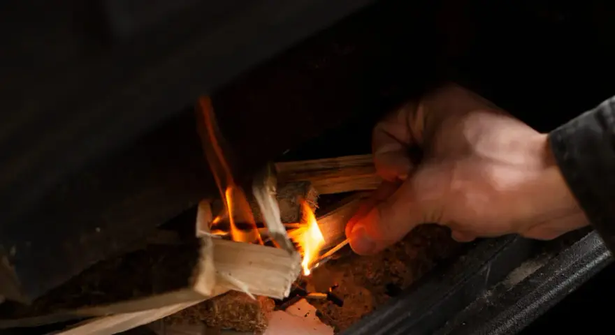 Main allumant un feu dans un poêle à bois avec une allumette.