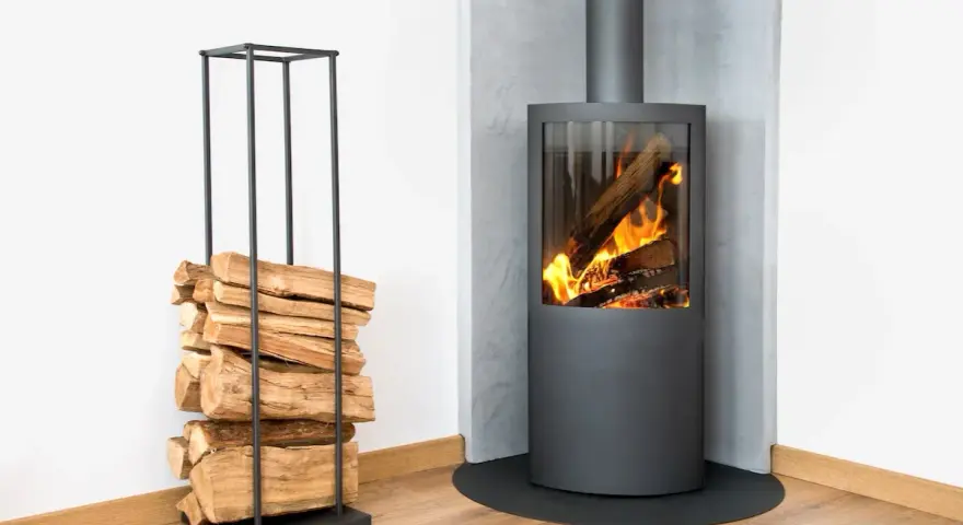 Un poêle à bois moderne, avec du bois empilé à côté, prêt pour le feu. Le placo mural met en valeur la distance parfaite pour la sécurité.