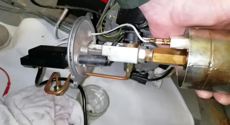 Main d'un technicien ajustant un composant de chaudière fioul en sécurité. Tuyaux en cuivre et raccords laiton visibles.