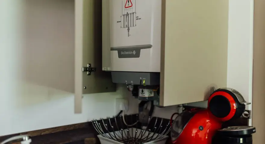 Chaudière gaz instantané De Dietrich installée dans un placard, à côté d'une machine à café rouge.