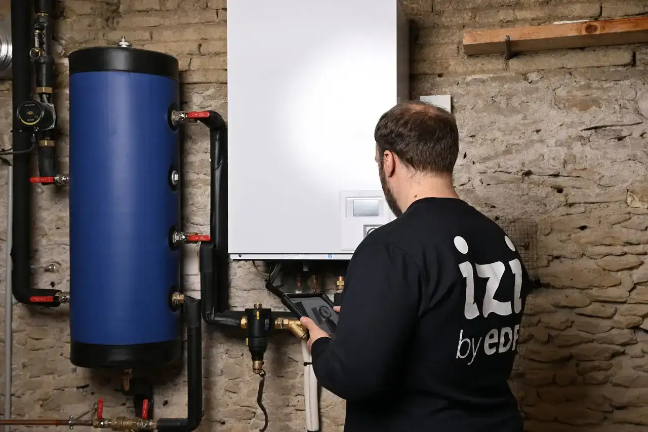 Un technicien vérifie une chaudière fioul en sécurité avec une tablette. L'installation comprend un ballon bleu et des tuyaux.