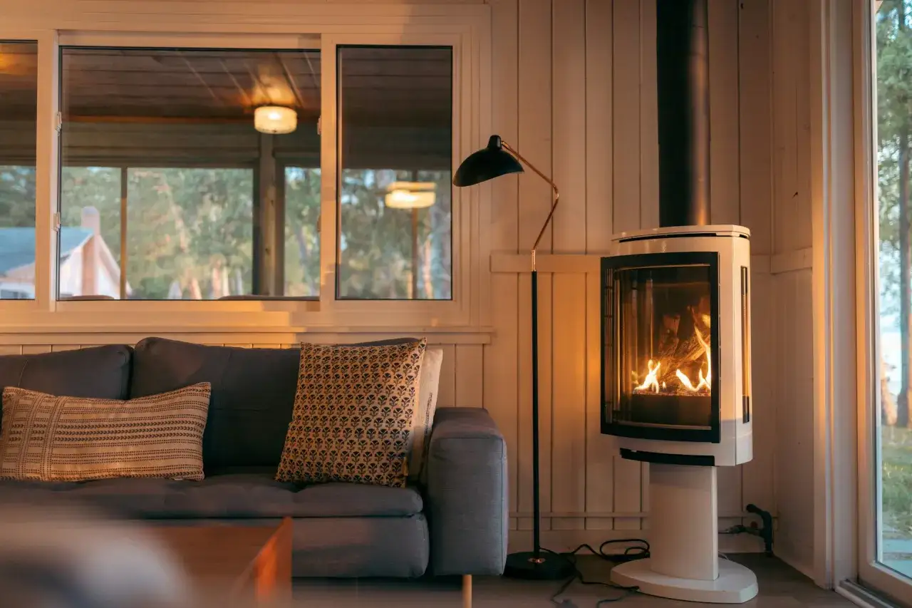 Un poêle à bois moderne, avec un feu vif, est placé à distance du mur en placo. Un canapé confortable invite à la détente.