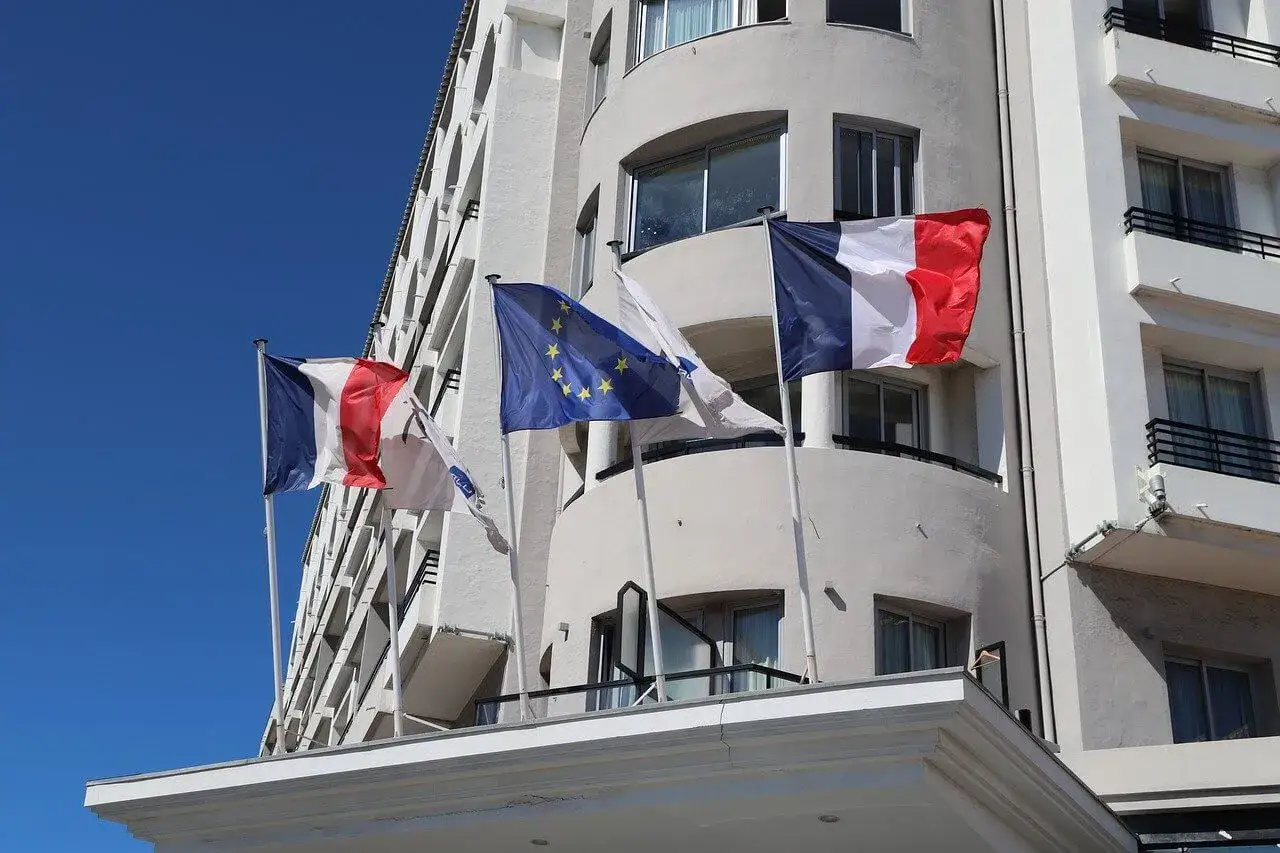 Drapeaux français et européen flottant devant un bâtiment blanc, symbole d'un projet de rénovation énergétique.