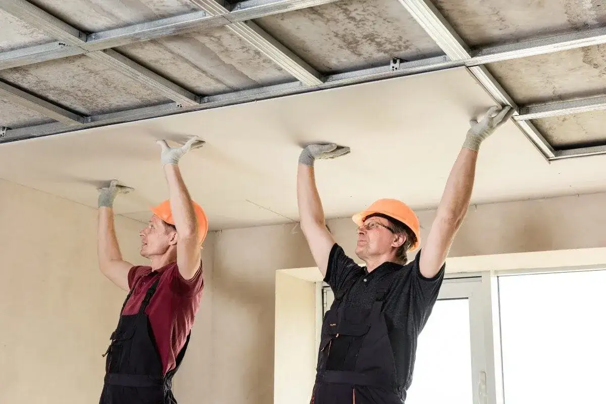 Deux ouvriers installent des plaques de plafond dans un garage, améliorant l'isolation.