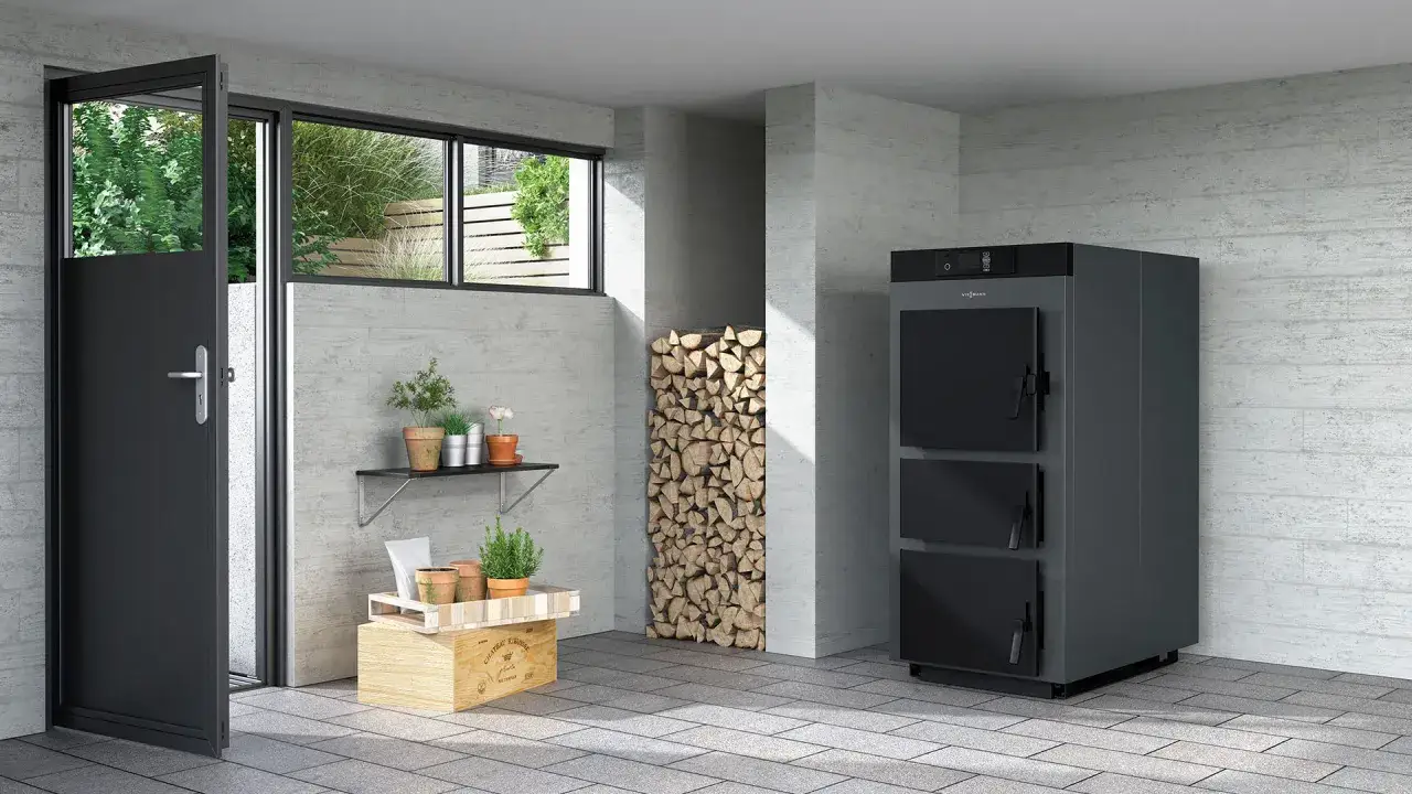 Une chaudière biomasse moderne, entourée de bois de chauffage, de plantes et d'une porte ouverte sur un jardin verdoyant.