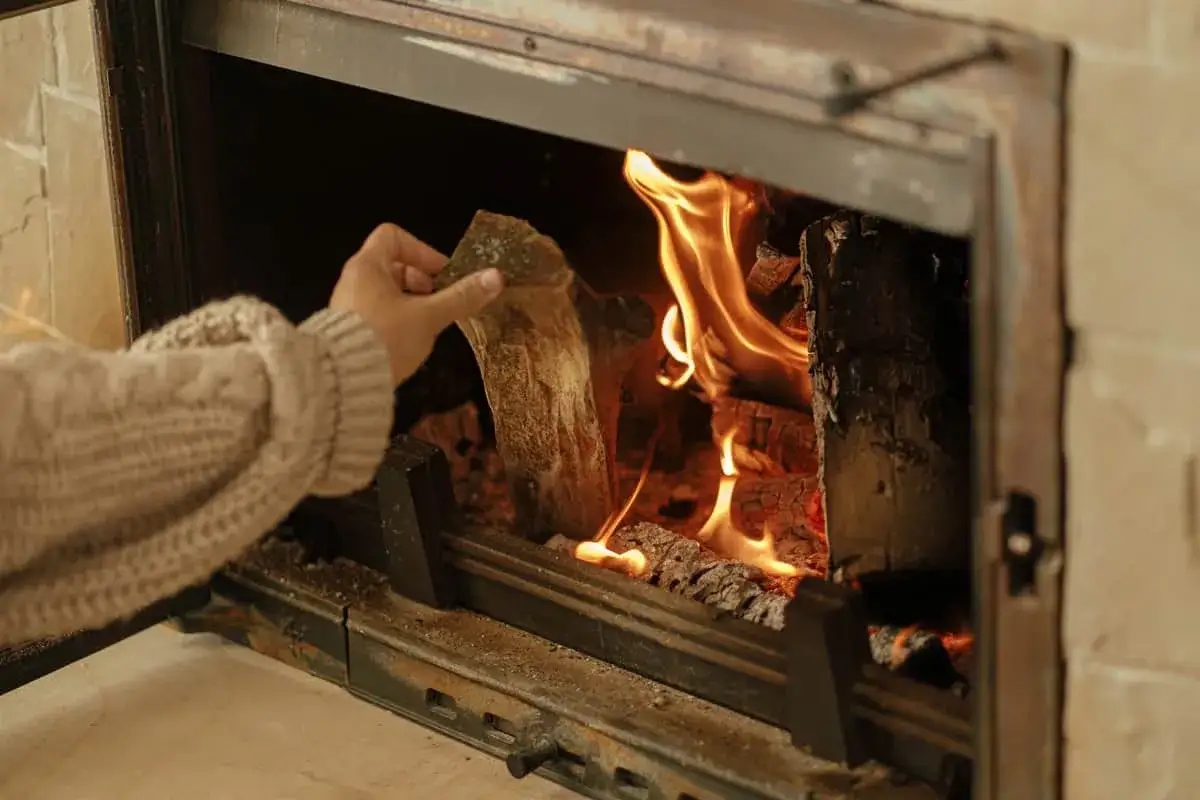 Main tenant ajoutant du bois dans un poêle, le deflecteur poele a bois assure une combustion optimale et une chaleur diffuse.