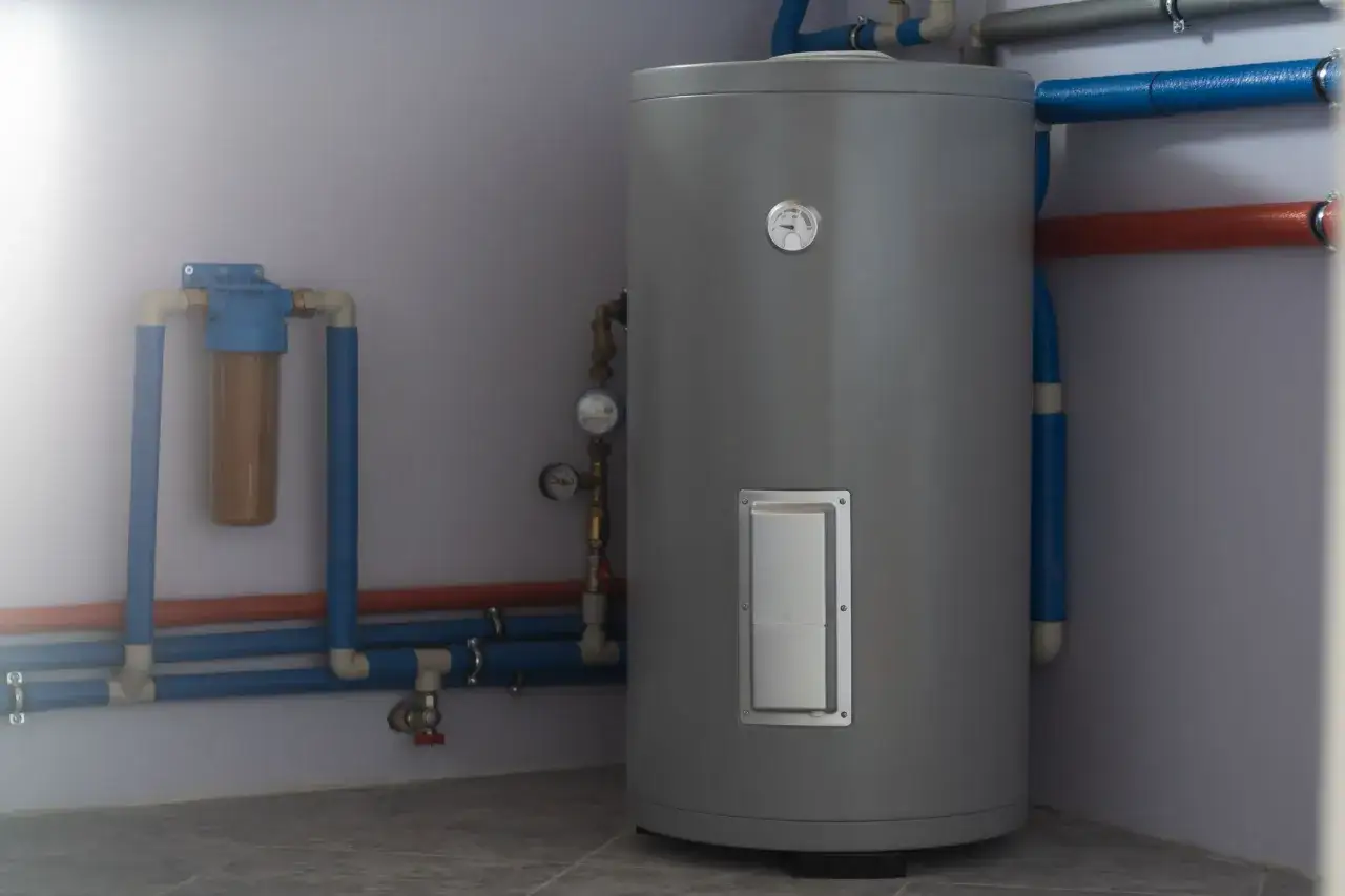 Un chauffe-eau gris avec un filtre à eau et des tuyaux bleus et rouges. Un guide pour comment choisir son chauffe eau.