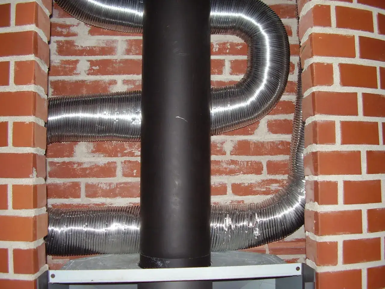 Mur brique réfractaire derrière poêle, avec gaines argentées. Installation de conduit de fumée.