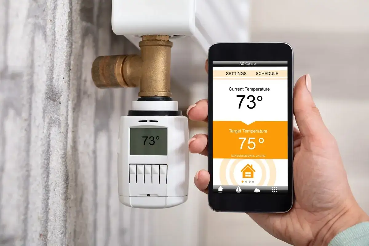 Une main tient un smartphone affichant un cee thermostat connecté. La température actuelle est de 73°, la cible est de 75°.