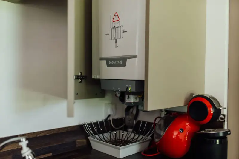 Chaudière gaz instantané De Dietrich installée dans un placard, à côté d'une machine à café rouge.