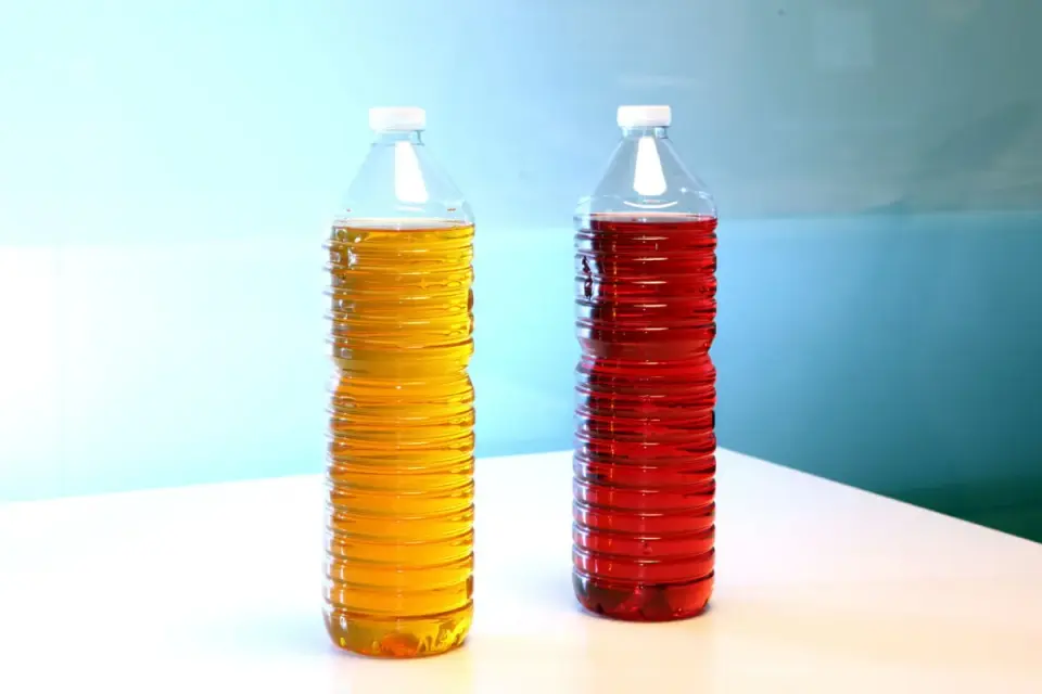 Deux bouteilles de fioul couleur, l'une jaune doré, l'autre rouge vif, se dressent sur une table blanche.